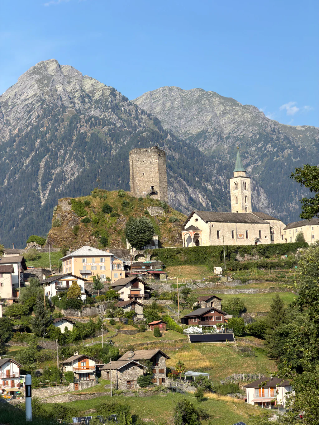 A stone tower and church beneath mountain peaks in a Swiss Alpine village