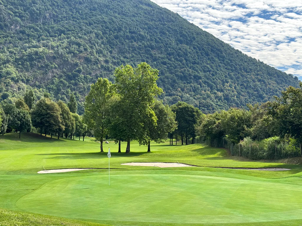 A quiet green fairway framed by steep Alpine mountains