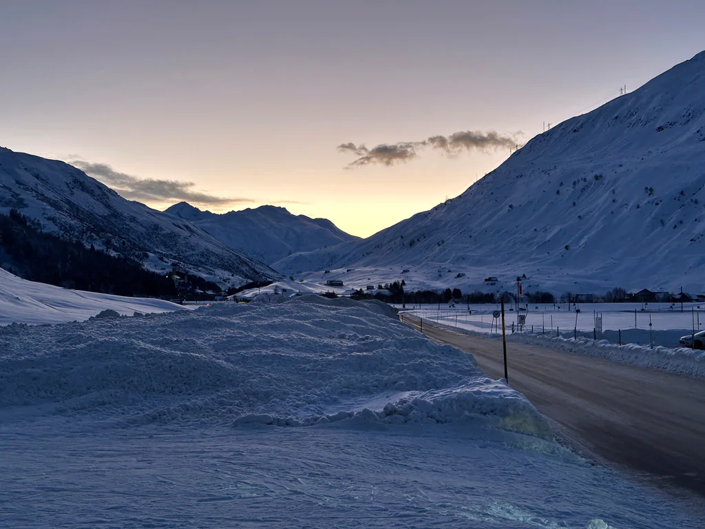 A snow-lined road leading into the Andermatt valley beneath the last twilight glow