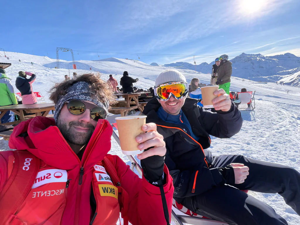 Peptone team members raising hot drinks beside the snowy ski slopes of Andermatt
