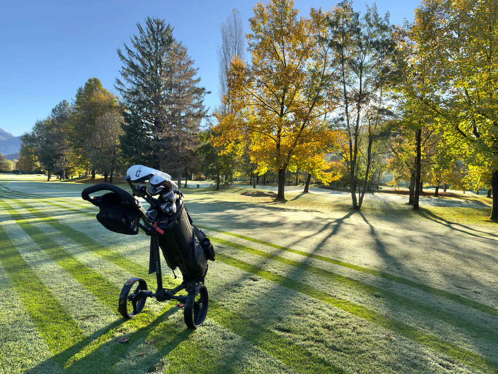 A golfer crossing a tree-lined fairway in crisp autumn light