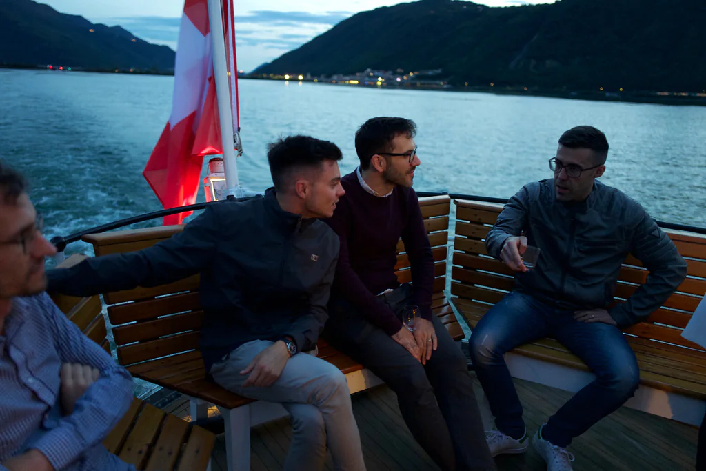 Peptone team members talking on the deck of a boat crossing Lake Lugano at dusk