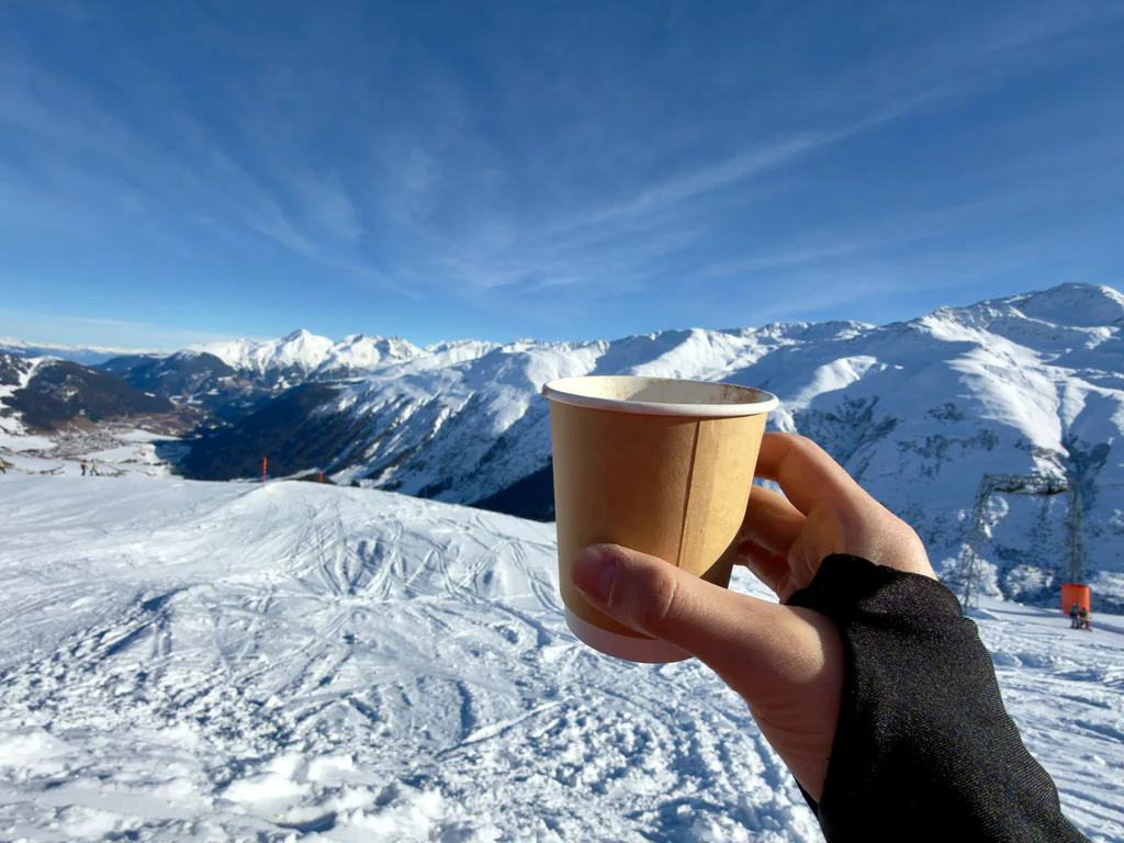 A cup held above the snow-covered mountains on a clear winter day